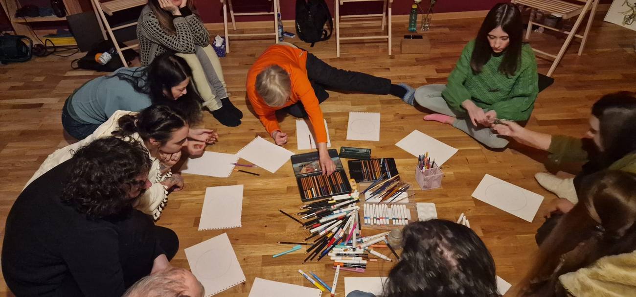 Grup de participanți desenând mandale pe podea